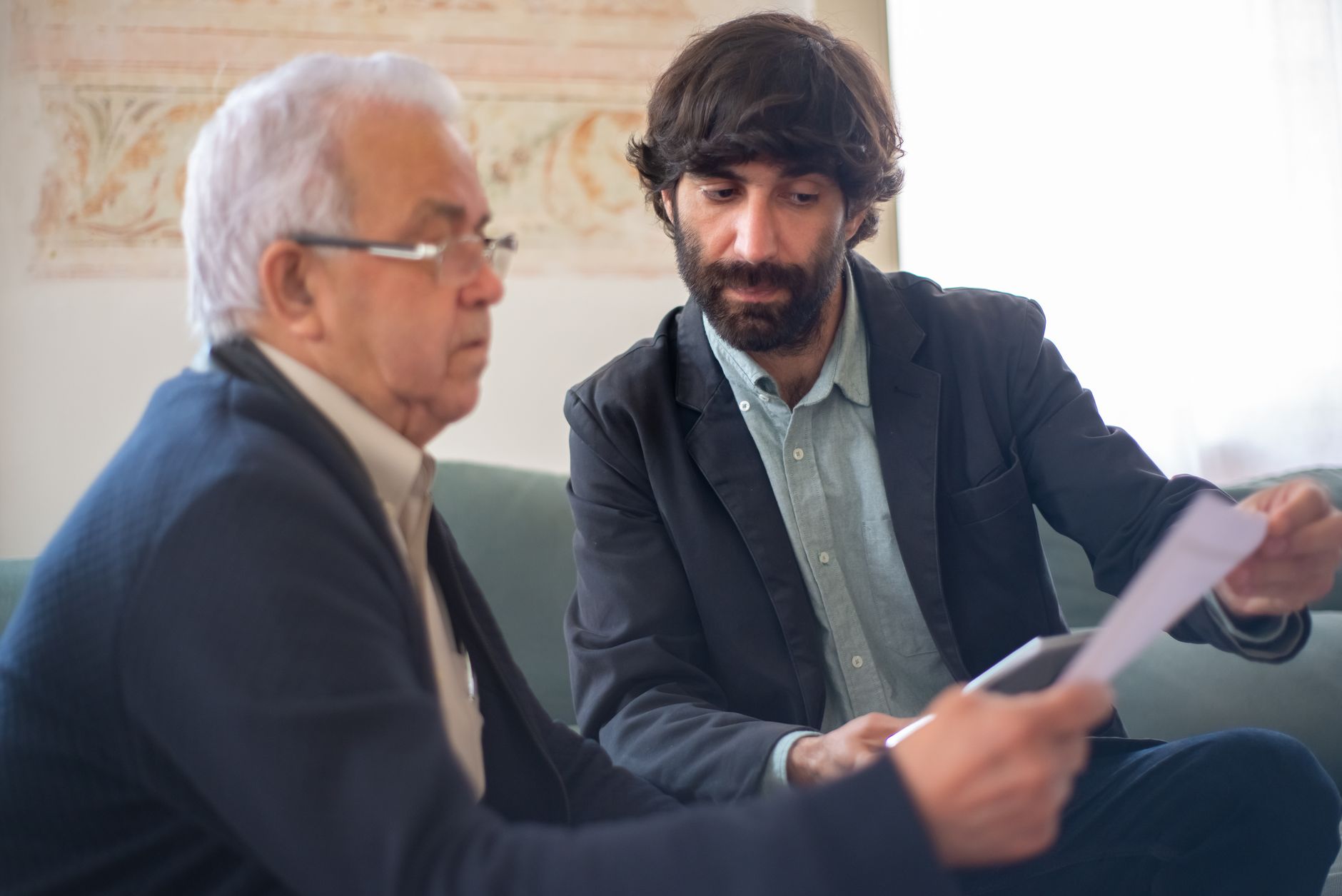 A broker going through a printed page with an older client on a sofa